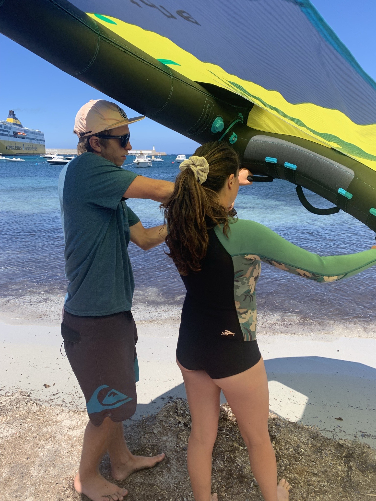 Moniteur Wingbox ajustant l'aile de wingfoil d'une élève dans la baie de L'Île-Rousse