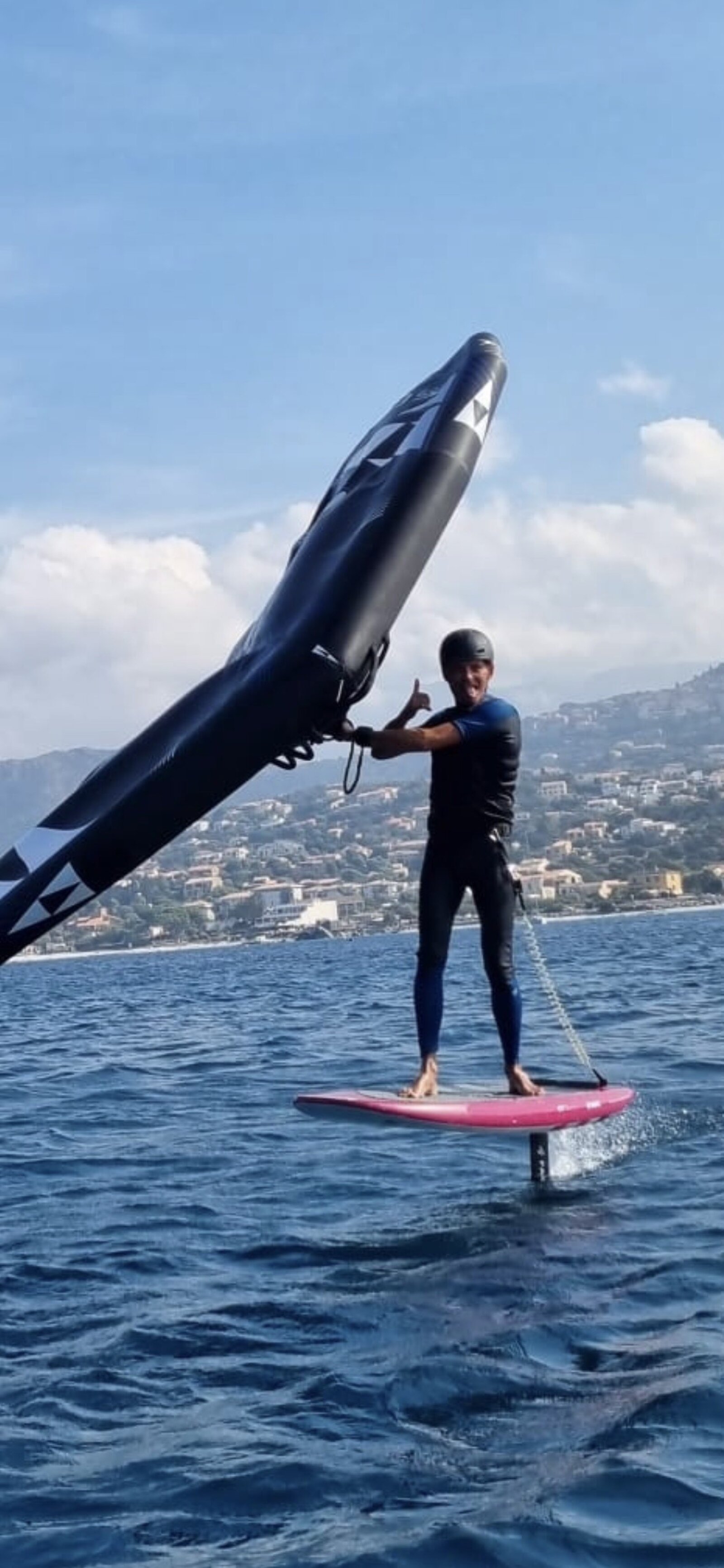 Moniteur Wingbox tenant une aile de wingfoil au-dessus de la baie de L'Île-Rousse